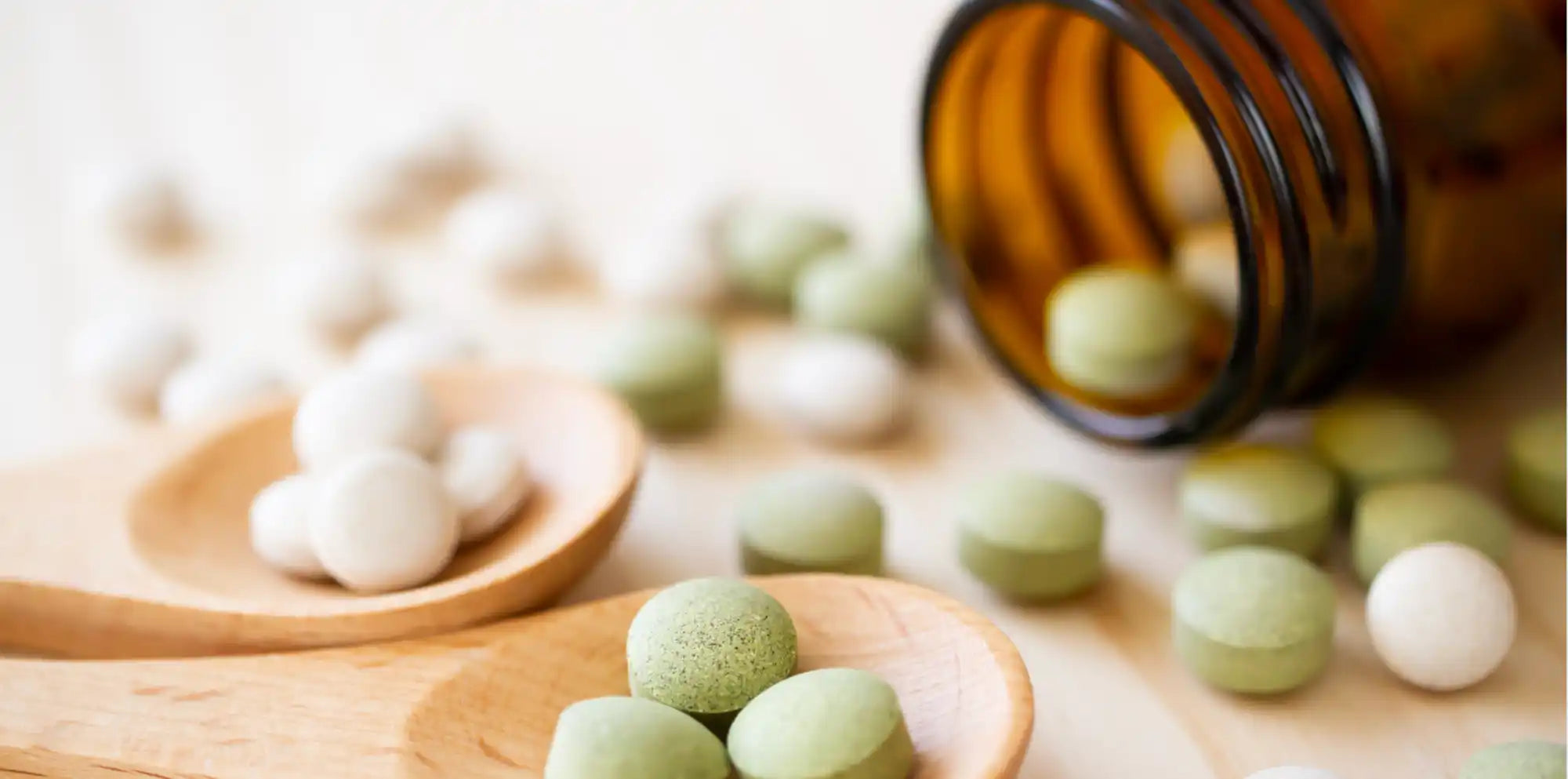 Tabletten in zwei Farben (weiß und grün) mit einigen in einer braunen Flasche und einige auf zwei Holzlöffeln.